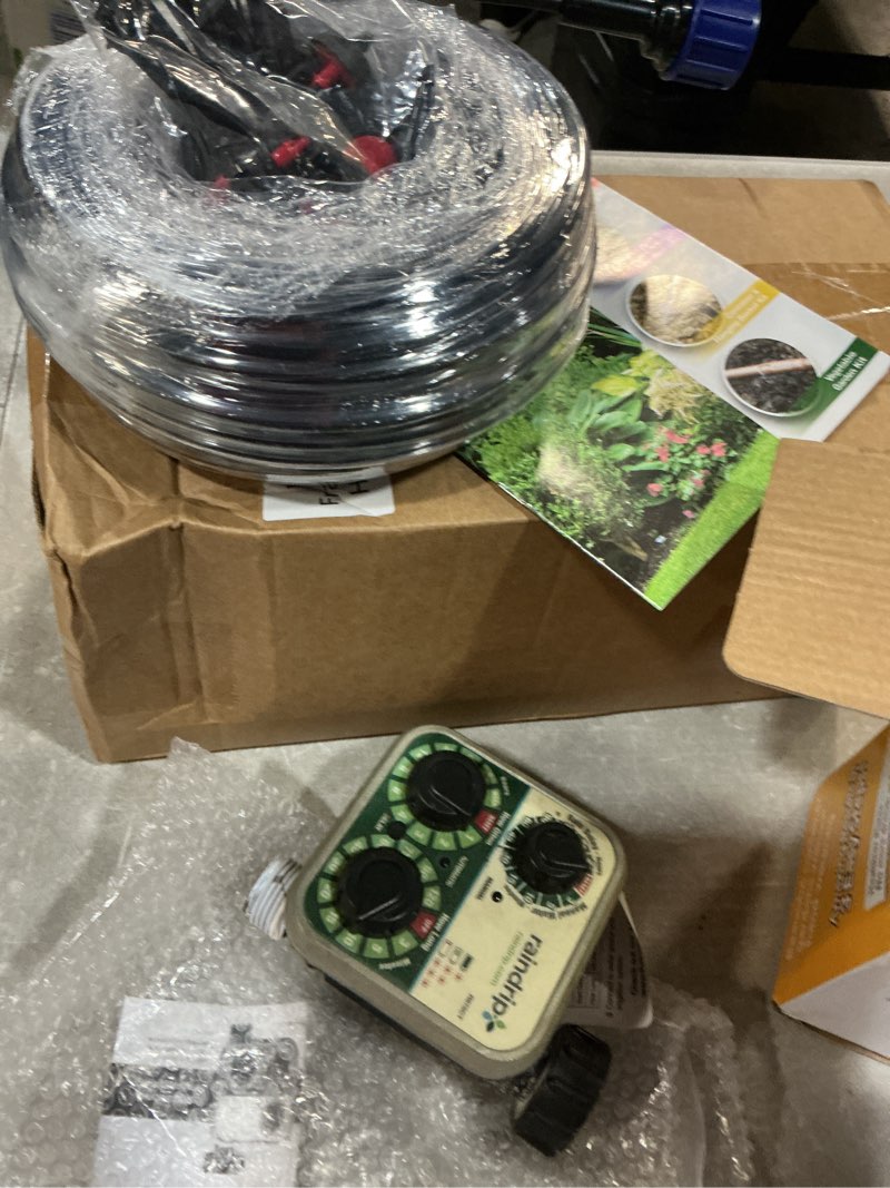 Condition photo showing As Is for raindrip r560dp drip watering system, automatic drip irrigation system with timer for containers and hanging baskets, waters up to 20 plants, includes 20 drippers, black container & hanging baskets timer