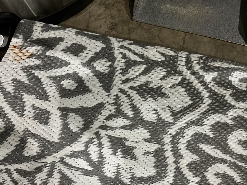 Condition photo showing As Is for reversible gray and white polypropylene outdoor scroll area rug
