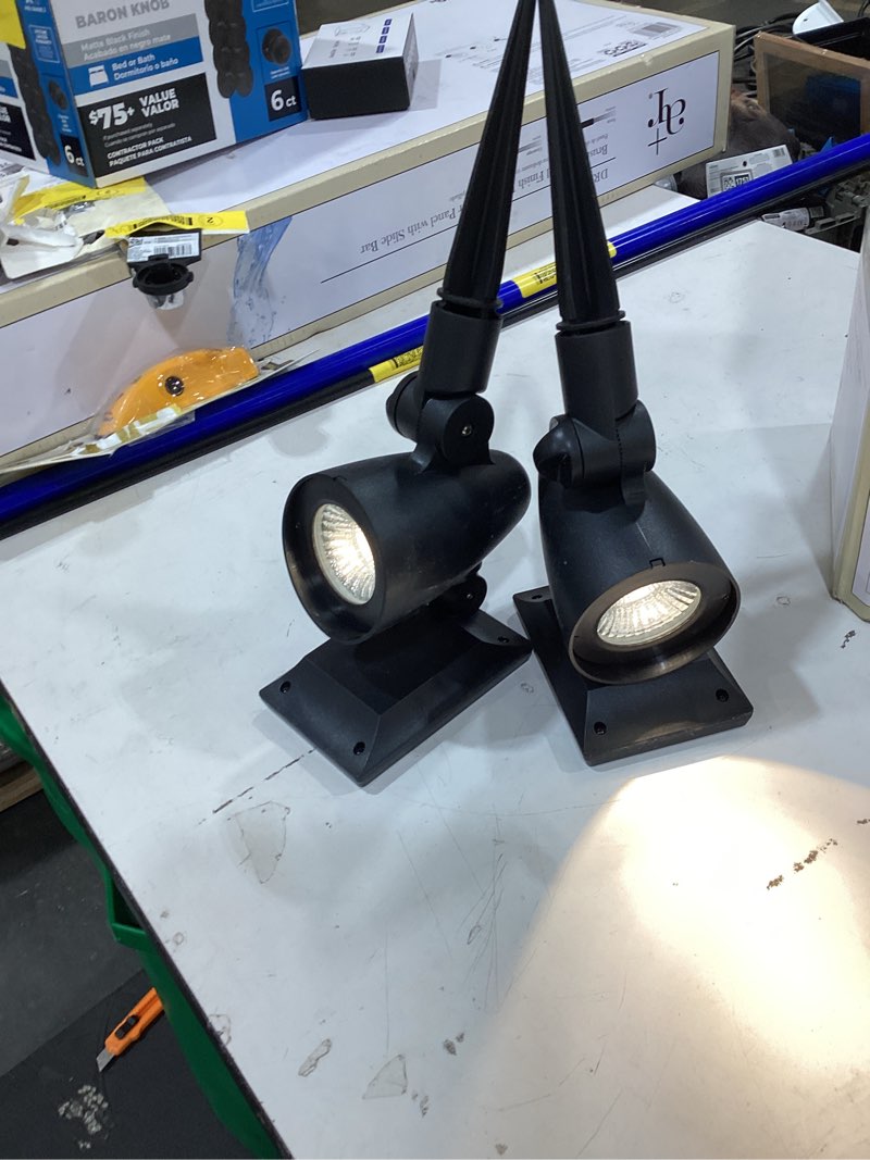 Condition photo showing As Is for 2-pack solar powered black led landscape spot lights – 30 lumens, warm white, auto dusk-to-dawn, outdoor use